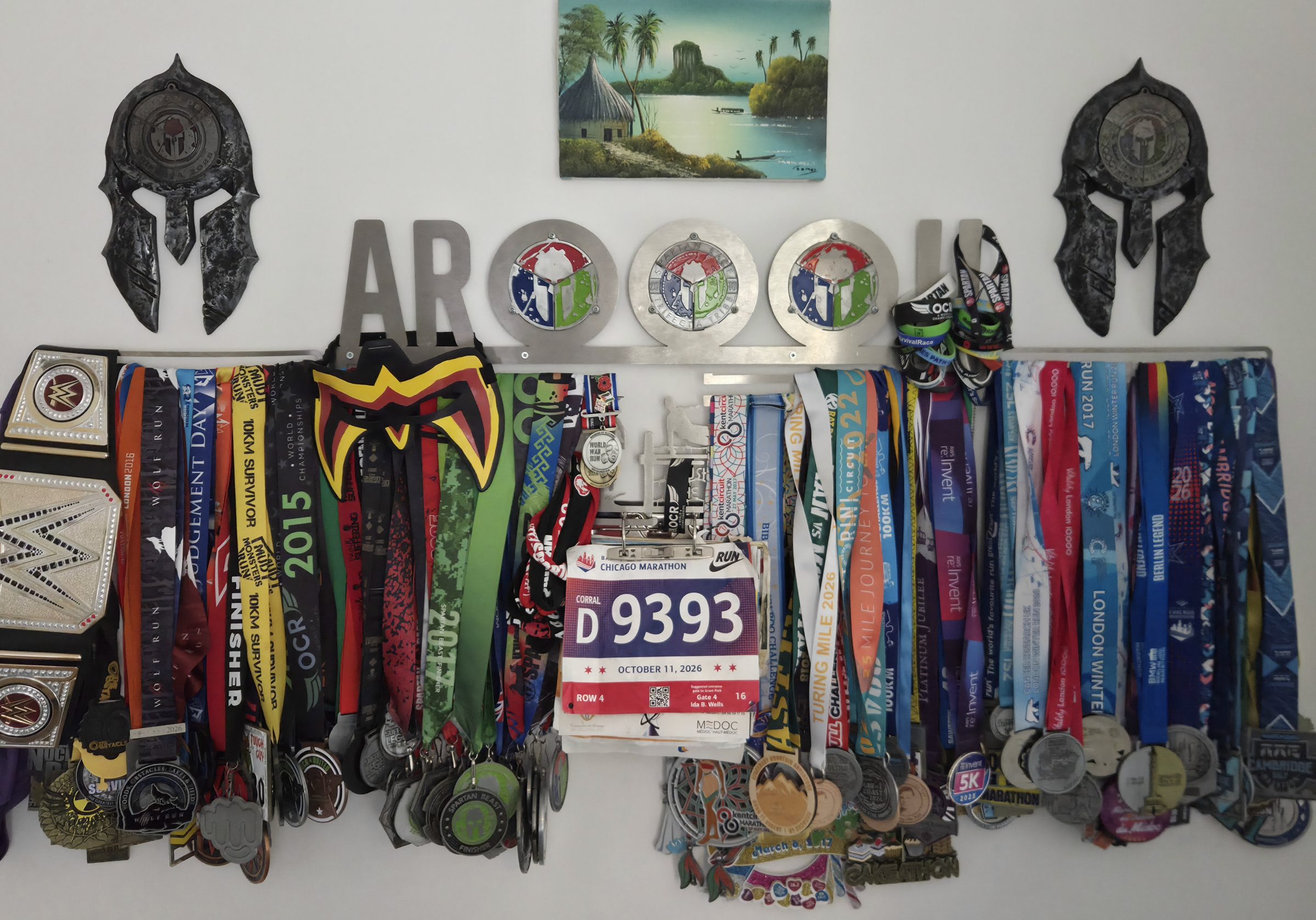 Dan's medal wall: rows of race medals and Spartan trifecta medals hanging under a painting