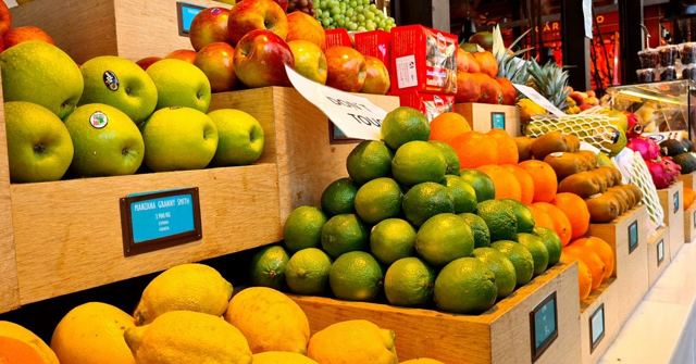 Crates of lemons, limes, apples and other fruit stacked at a colourful market stall.
