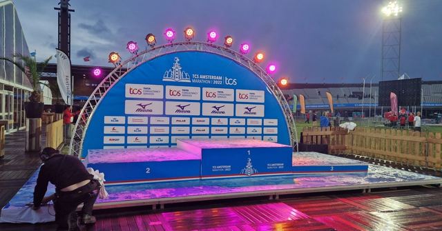 A brightly lit marathon podium stage with an arch of lights, with a worker setting up.