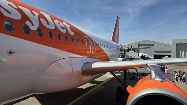 Close view of an orange and white easyJet plane nose and engine on a sunny airport apron.