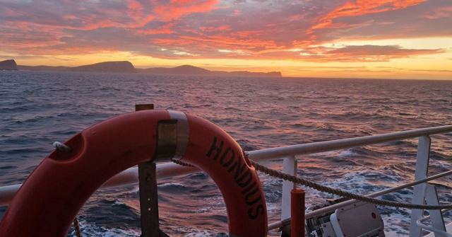 Vivid orange sunset over the sea seen from a ship's deck with a red and white lifebuoy.