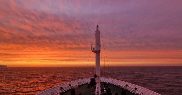 Fiery orange and red sky over the sea seen from a ship's bow and mast.