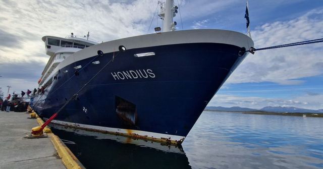 Blue-hulled expedition ship named Hondius moored at a quay under a cloudy sky.