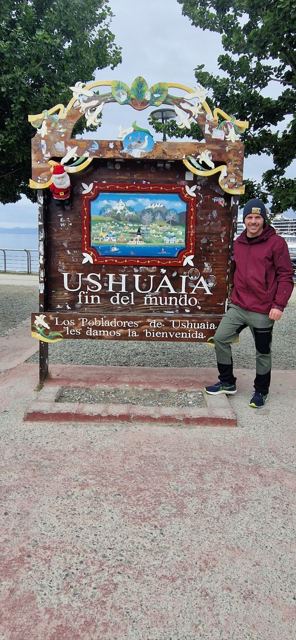 A man standing next to the colourful Ushuaia end-of-the-world sign.