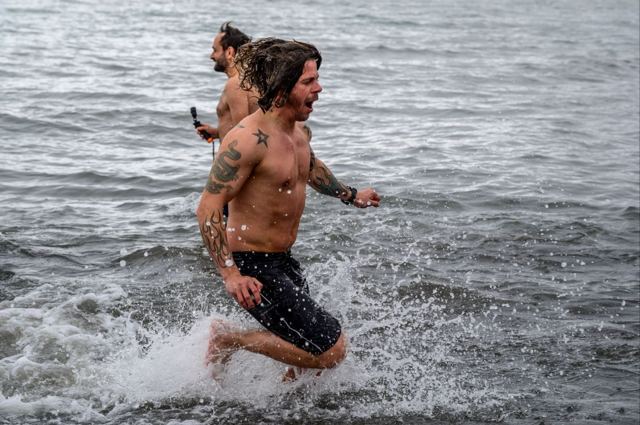 A shirtless man splashing out of icy grey sea water at Deception Island.