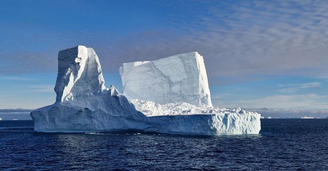 Large white iceberg with flat top and sheer sides floating in deep blue water.