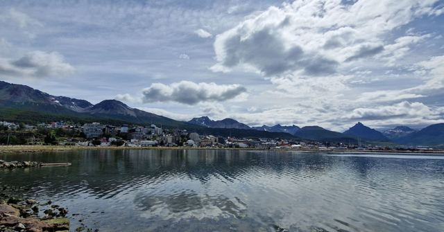Small town along a calm bay reflecting mountains and clouds.