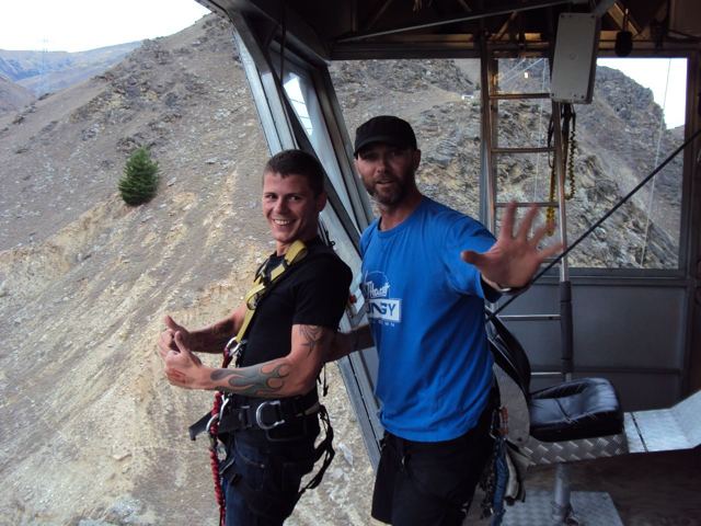 Two men in harnesses posing in the cable car above a canyon at the Nevis Swing.