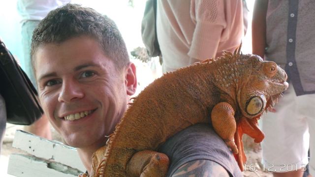 A smiling man with a large orange iguana resting on his shoulder.