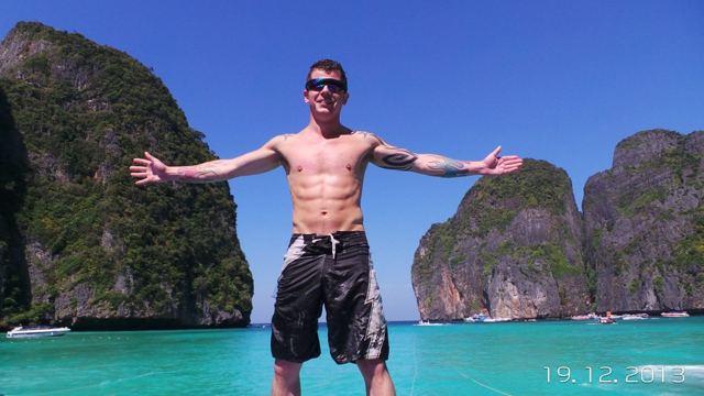 A man with arms outstretched standing in turquoise water between towering limestone islands.