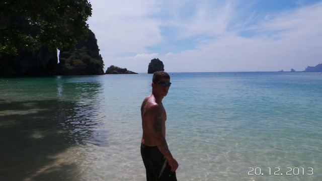 A man standing in clear shallow sea water with limestone islands in the background.