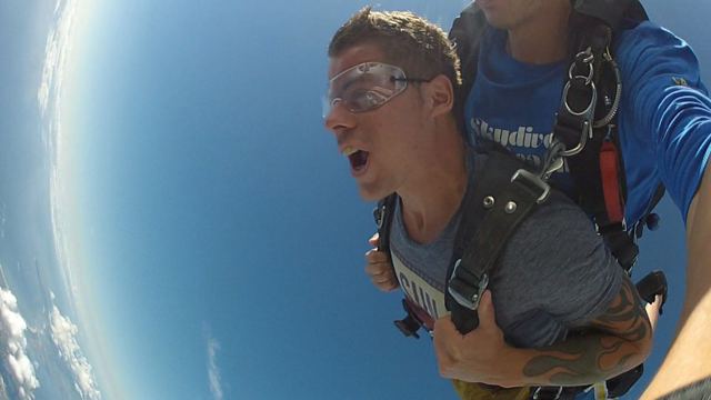 A man in goggles and a harness free-falling with the curved horizon and sea below.