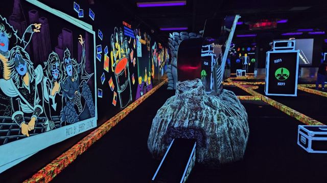 Glow-in-the-dark mini golf course with neon blacklight murals and a sculpted rock obstacle.