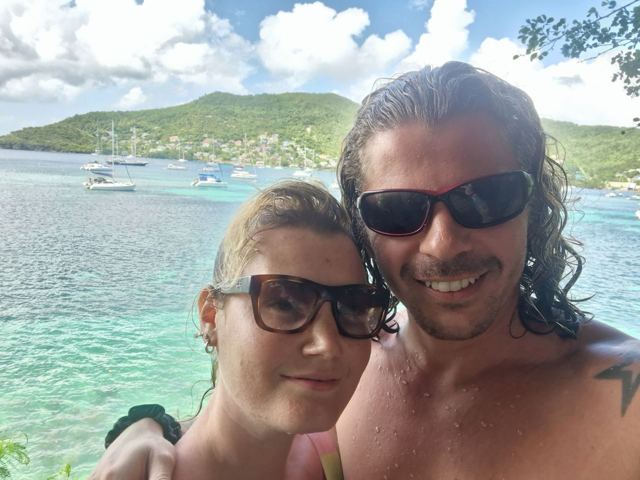 A man and a woman taking a selfie above a turquoise bay with boats.