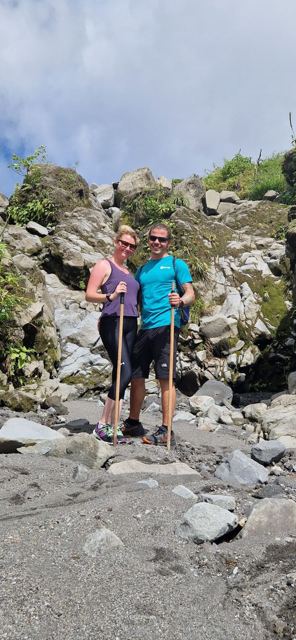 A man and a woman with walking sticks standing among rocks in the rainforest.