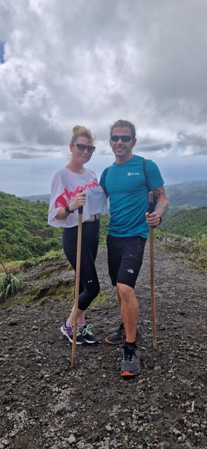 A man and a woman with wooden walking sticks on a ridge above green hills.