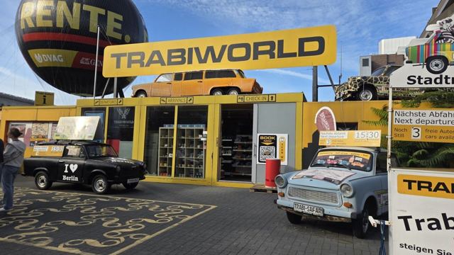 Colourful Trabant cars parked outside a yellow Trabi World building with a large sign.