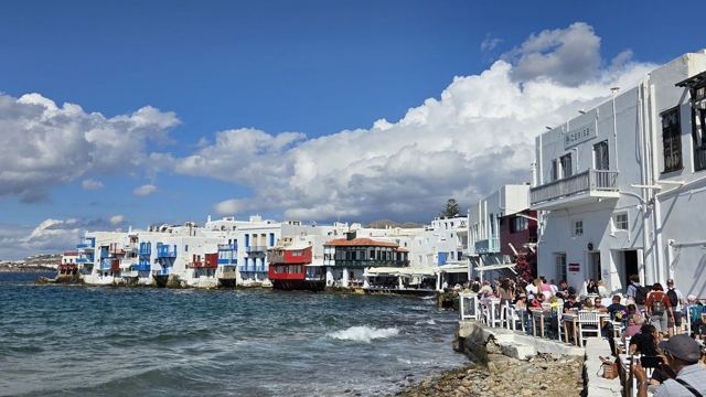 White houses with colourful balconies built right at the water's edge under blue sky.