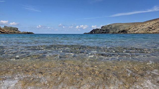 Crystal-clear shallow water over pebbles in a cove with rocky headlands.