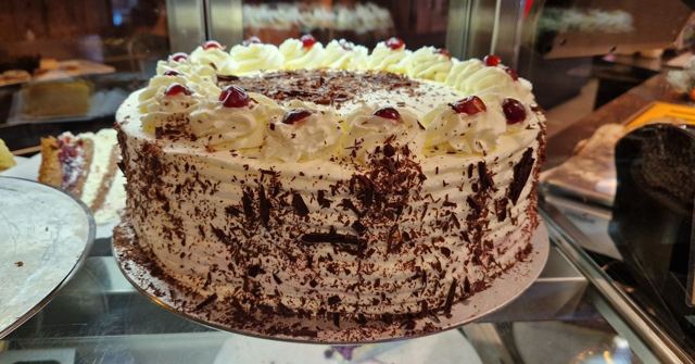 A whole Black Forest gateau topped with cream and cherries, covered in chocolate shavings.