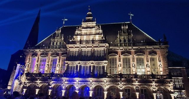 Bremen's ornate Renaissance town hall illuminated at night against a deep blue sky.