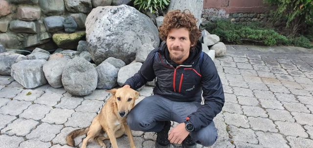A man crouching on a stone path beside a friendly brown dog.