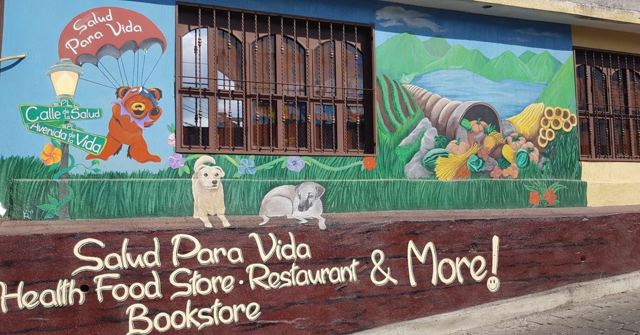 A shop front with a painted mural and a sign reading Salud Para Vida health food store and bookstore.
