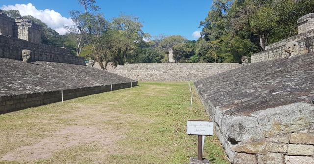 A grassy Mayan ball court flanked by sloping stone walls at the Copan ruins.