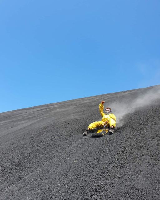 A person in a yellow jumpsuit sliding down a steep black volcanic ash slope.