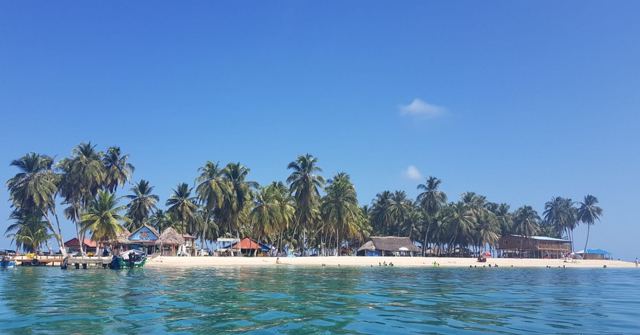 A small palm-fringed island with a white sand beach surrounded by turquoise water.