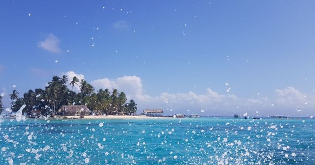 Water droplets flying in front of a small palm-covered island on bright turquoise sea.