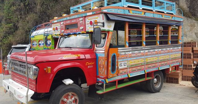 A vividly painted chiva bus with a red front parked on a street.