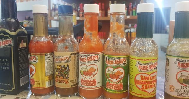 A row of bottles of colourful Belizean hot sauce lined up on a shelf.