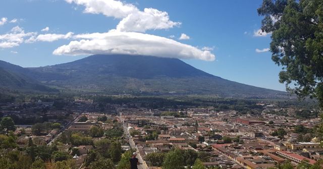 A cone-shaped volcano with a cap of cloud above the town of Antigua Guatemala.