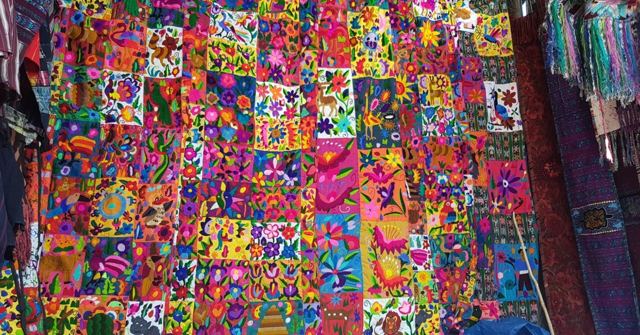 A large colourful embroidered textile with floral patterns displayed at a market.