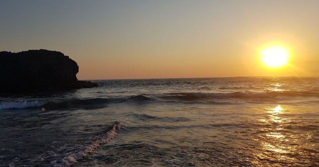A golden sunset over ocean waves with a dark rocky headland on the left.