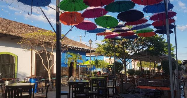 Colourful umbrellas suspended above outdoor café tables on a sunny street.