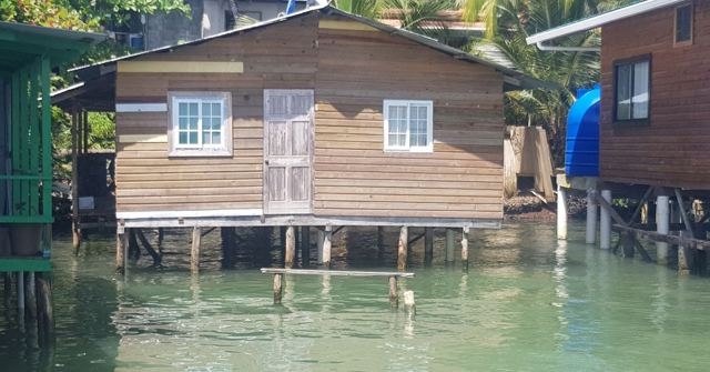 Wooden stilt houses built over calm clear green water.