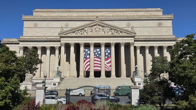 A grand columned government building with a large American flag banner hanging between the columns.