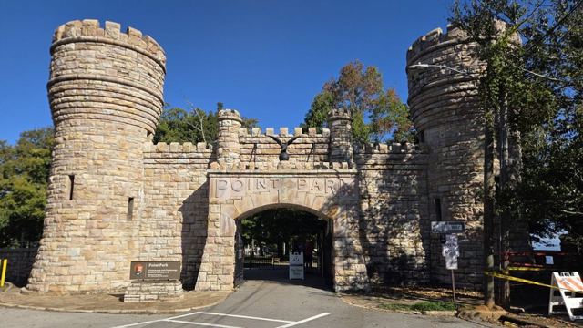 Stone castle-style gateway with two turrets and an arched entrance under a blue sky.
