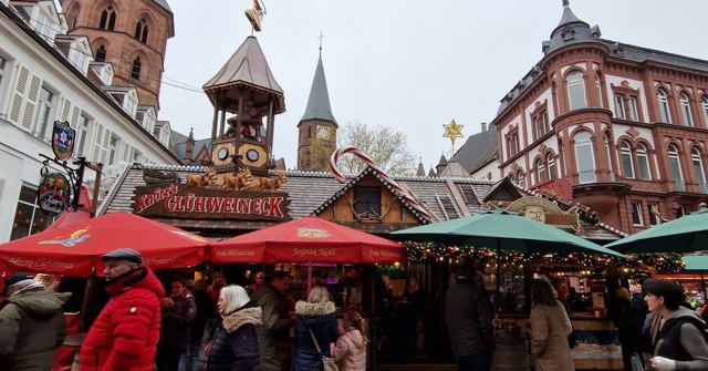 A busy Christmas market with wooden stalls, red umbrellas and historic buildings behind.