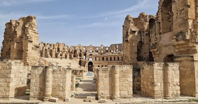 Ruined interior of a Roman amphitheatre with stone arches and tiers of seating.