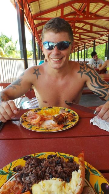 A smiling man in sunglasses at a table with a plate of seafood and rice.