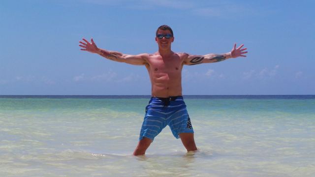 A man standing with arms outstretched in shallow turquoise water.