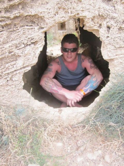 A man in sunglasses crouching inside a hole cut into pale rock.