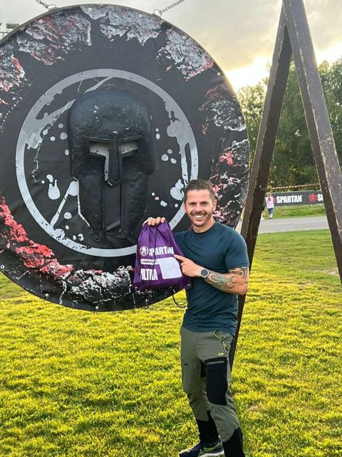 A man holding a race kit bag in front of a giant Spartan shield.