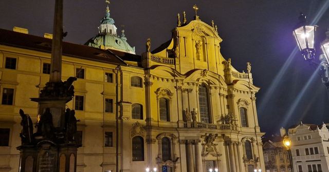 Ornate baroque church illuminated at night beside a street lamp and a statue.