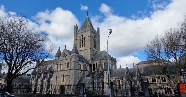 A grey stone Gothic cathedral with a tall tower under a blue sky with white clouds.