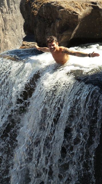 A man leaning over the edge of Devil's Pool with water pouring over Victoria Falls.