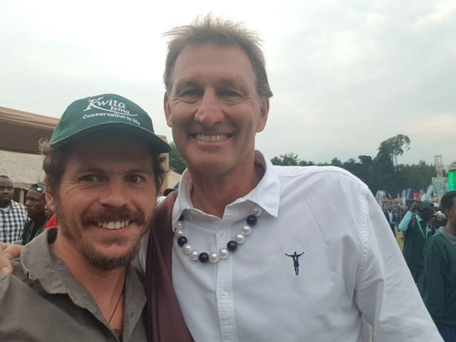 Two smiling men taking a selfie in a crowd at an outdoor ceremony in Rwanda.